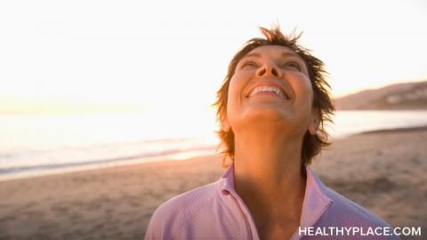 A woman is at the beach with her head turned toward the sky smiling