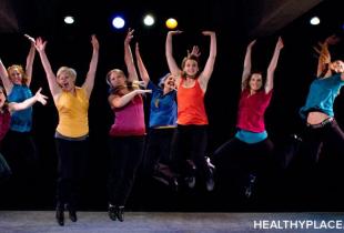 eight women in bright shirts are jumping with arms up on a stage